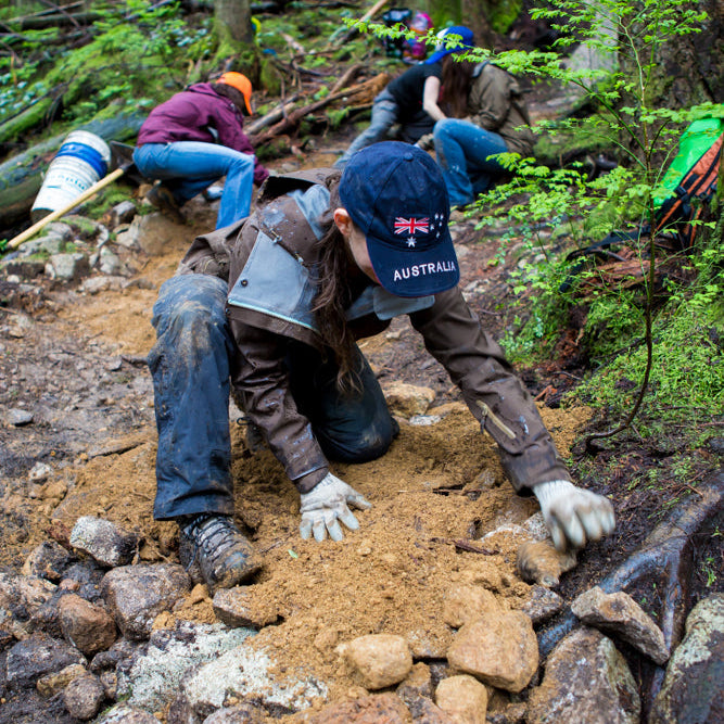People working on a trail in a forest, with one person wearing an Australian flag cap.