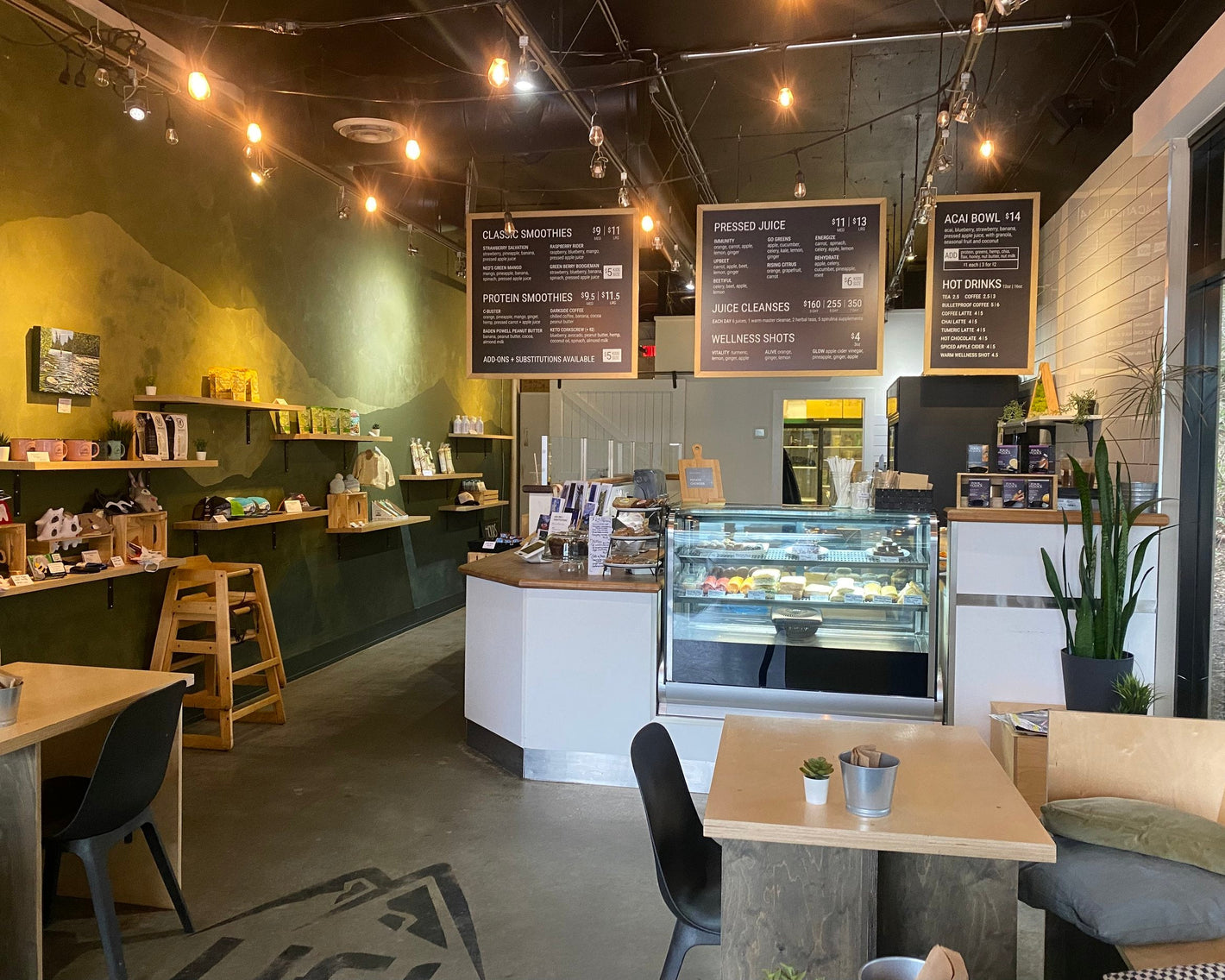Interior of a modern cafe with tables, chairs, and a display case.